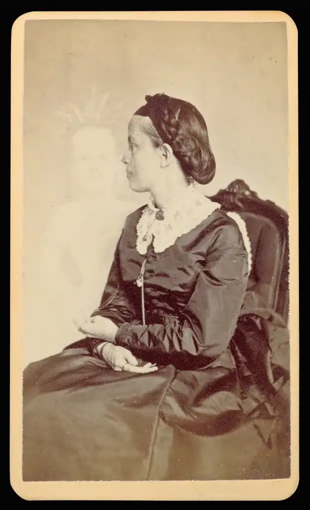 椅子に座る女性の背後に、光を放つ子どもの姿が半透明に写り込んだ古い写真