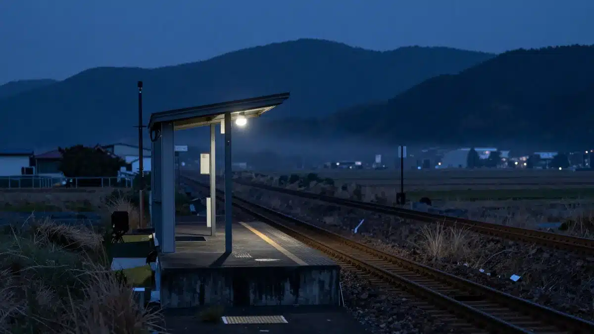 夜の山あいにある小さな無人駅のホームと、霧の奥へ続く線路